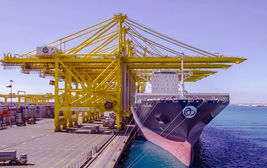 Efficient cargo handling at Jebel Ali Free Zone, a pivotal hub for company formation in Dubai. A vibrant yellow gantry crane dominates the scene, servicing a large container ship under a clear blue sky.